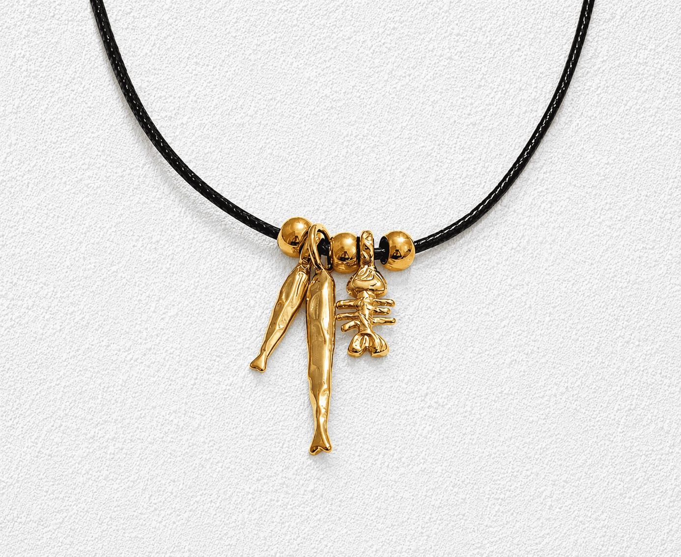MAR DE CALETA · Collar de cuero negro con dijes de pez y figura marina en oro.